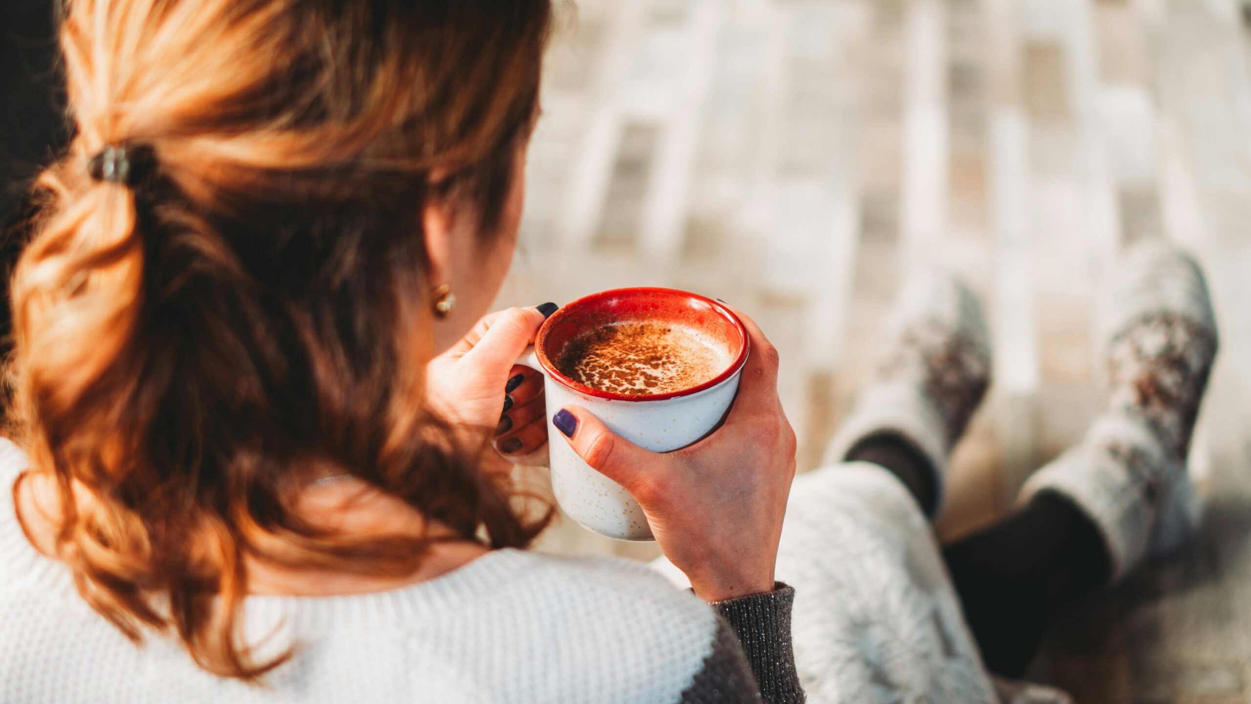 A woman sits comfortably indoors, holding a warm cup of coffee, perfect for a cozy break.
