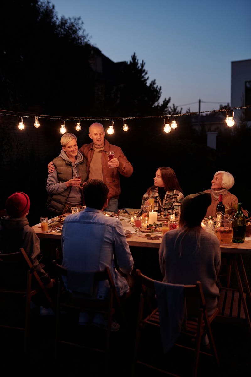 A warm family gathering during dusk, sharing dinner in a beautifully lit backyard setting.